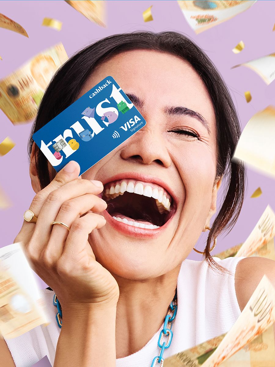 A woman laughing behind a Trust cashback Visa card as banknotes rain down.