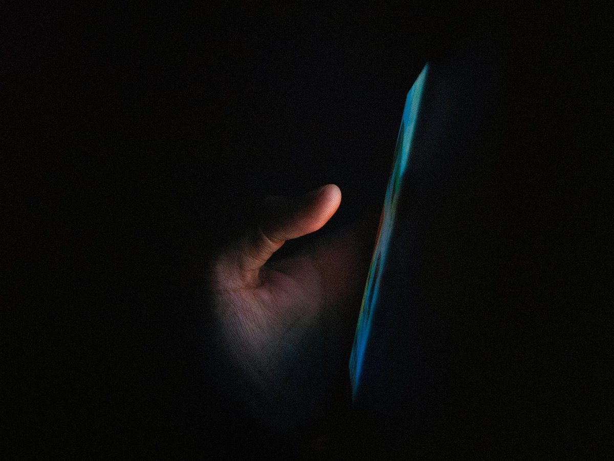A hand in the dark, lit by the glow of a phone screen.