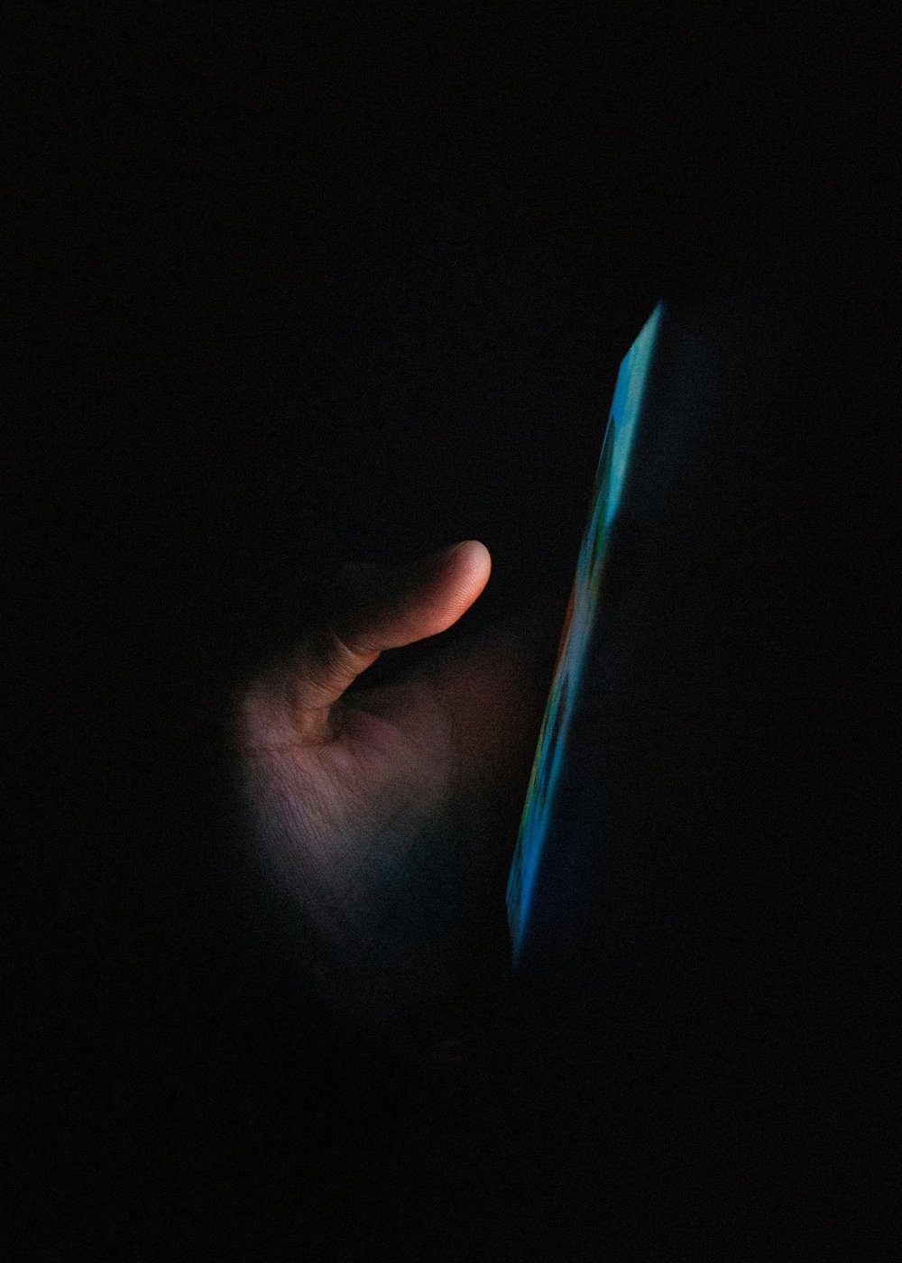 A hand in the dark, lit by the glow of a phone screen.