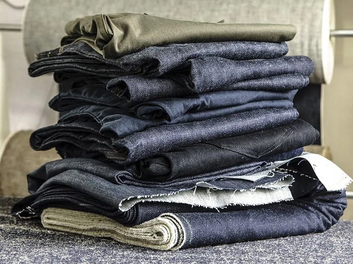 Folded raw selvedge denim stacked in front of bolts of fabric.
